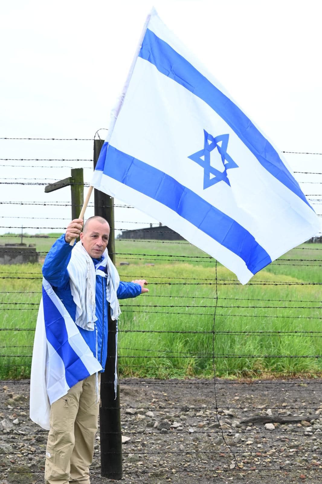 אופיר אלקלעי אוחז בגדר התיל במחנה אושוויץ עטוף בדגל ועם דגל ישראל מונף